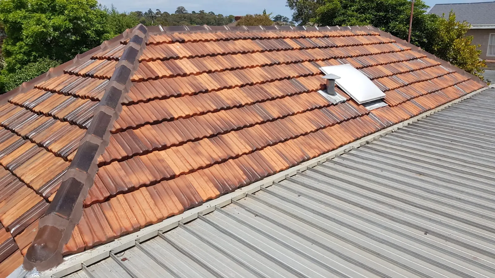 Terracotta tiled roof with ridge capping and roof penetration details visible